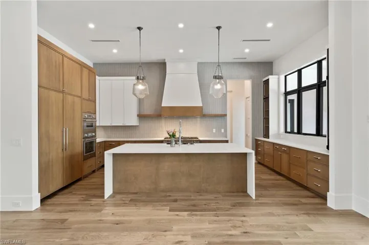 Kitchen with decorative light fixtures, custom exhaust hood, a center island with sink, and light hardwood / wood-style flooring