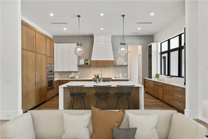 Kitchen featuring pendant lighting, custom exhaust hood, white cabinets, a center island with sink, and hardwood / wood-style flooring