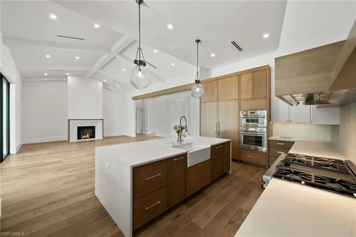 Kitchen featuring an island with sink, sink, appliances with stainless steel finishes, beam ceiling, and light hardwood / wood-style floors