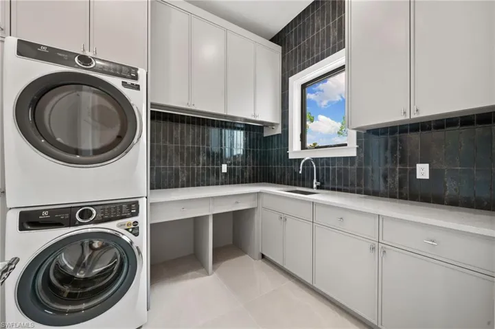 Clothes washing area featuring light tile patterned flooring, cabinets, stacked washer / drying machine, and sink