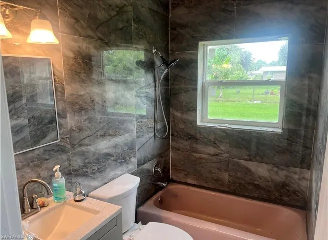 Full bathroom featuring contemporary wall tile, a window, and a built-in bathtub with a shower fixture