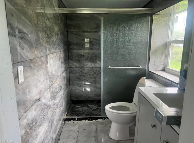 Bathroom featuring full-height stone-look tile, a sliding glass shower enclosure, and a vanity with a white countertop and integrated sink
