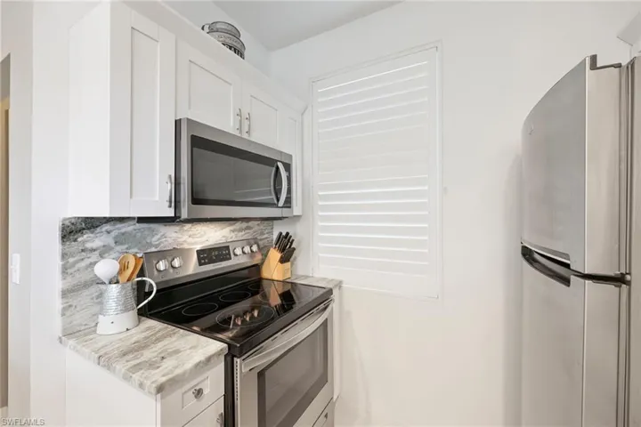 Kitchen with backsplash, white cabinetry, light stone counters, and appliances with stainless steel finishes