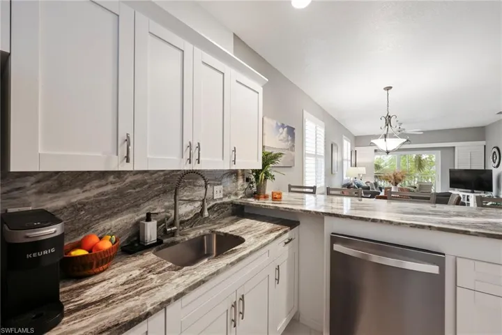 Kitchen with dishwasher, sink, decorative backsplash, light stone counters, and white cabinetry