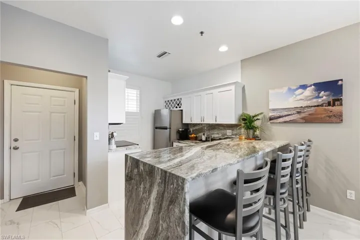 Kitchen featuring stainless steel refrigerator, light stone countertops, kitchen peninsula, a breakfast bar area, and white cabinets