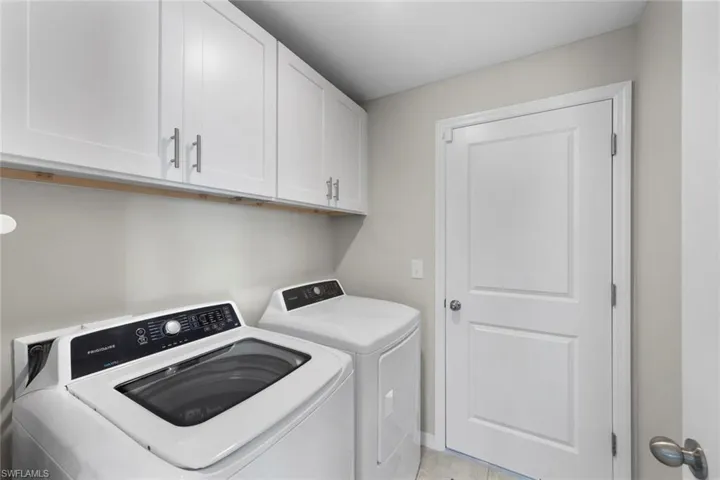 Clothes washing area with cabinets, washing machine and dryer, and light tile patterned floors