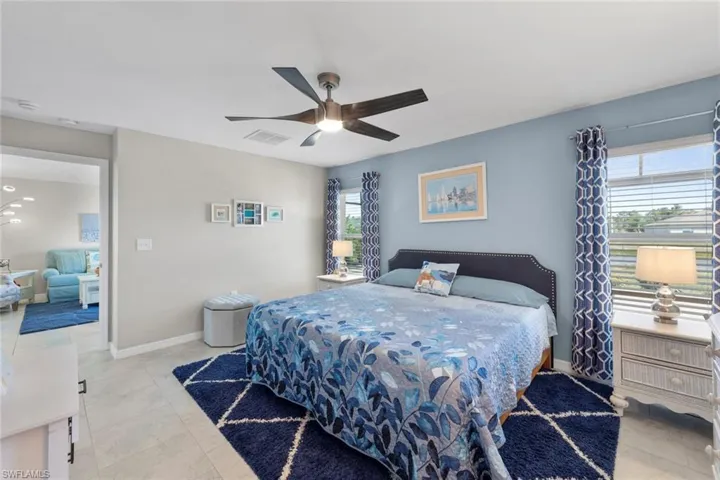 Primary bedroom with multiple windows, light tile patterned floors, and ceiling fan