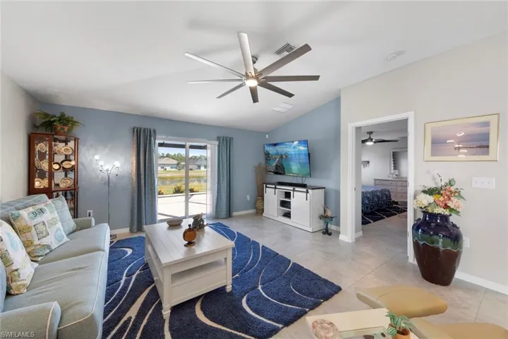 Living room featuring light tile patterned flooring, ceiling fan, and vaulted ceiling