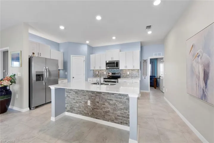 Kitchen with SS appliances, island with sink, white cabinets, and backsplash