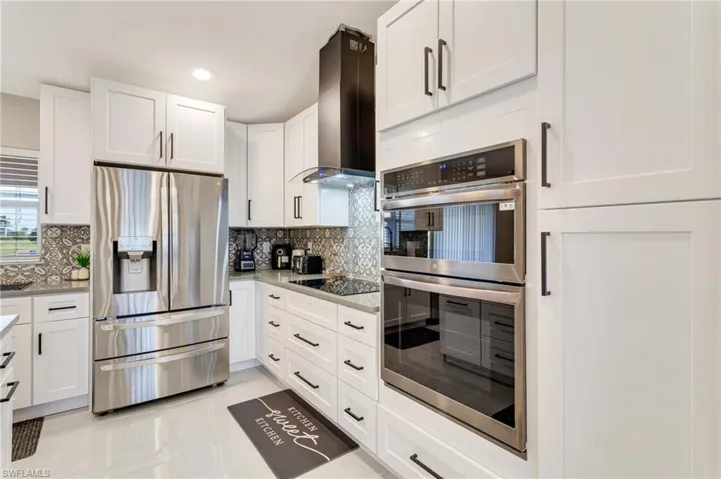 Kitchen featuring exhaust hood, white cabinets, recessed lighting, stainless steel appliances, and backsplash
