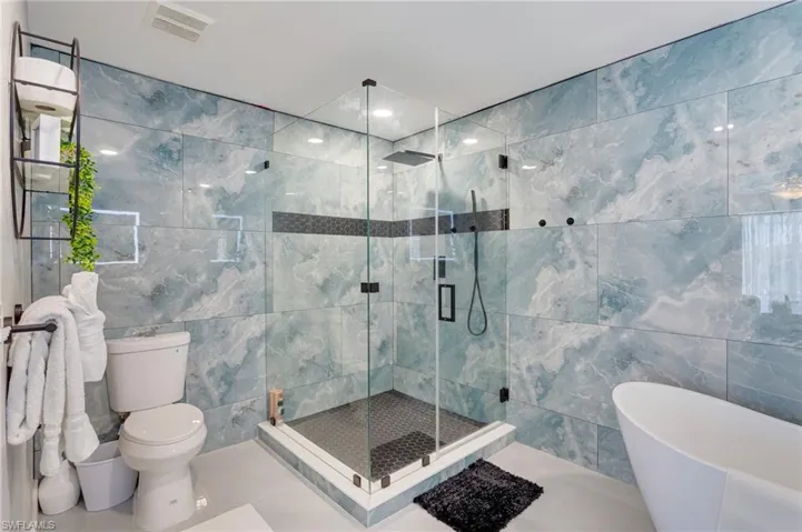 Full bath with visible vents, a freestanding tub, toilet, tile walls, and a stall shower