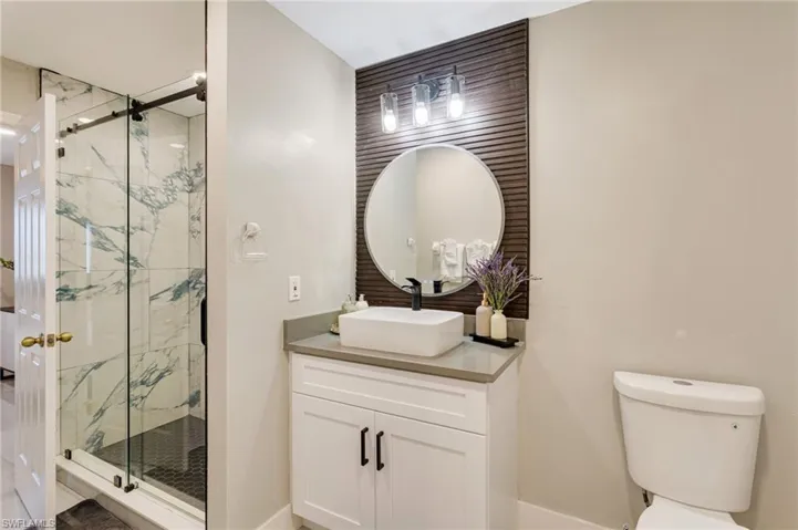 Bathroom featuring toilet, vanity, and a marble finish shower