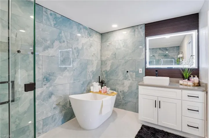 Bathroom with an enclosed shower, vanity, tile walls, and a soaking tub