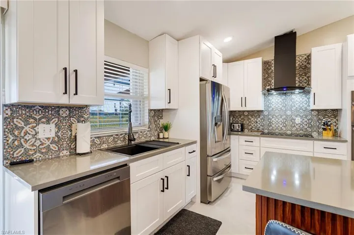 Kitchen with wall chimney range hood, white cabinetry, a sink, and appliances with stainless steel finishes