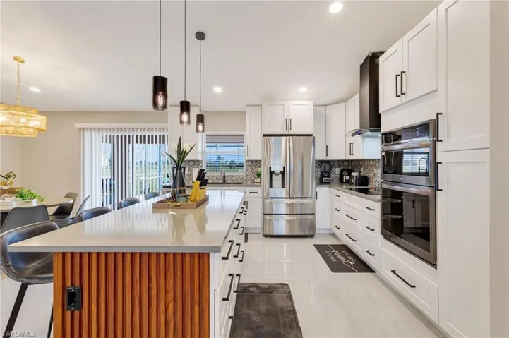 Kitchen with wall chimney exhaust hood, a sink, stainless steel appliances, a breakfast bar area, and backsplash