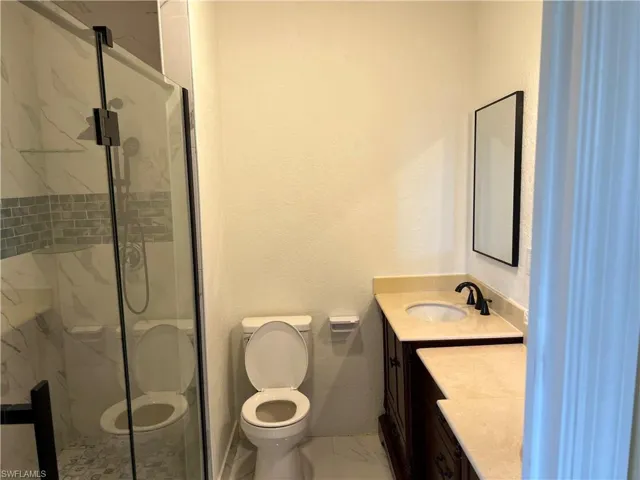 Full bathroom featuring a marble finish shower, toilet, marble finish floor, and vanity
