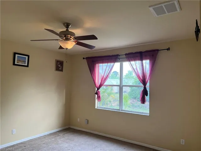 Empty room featuring carpet flooring, a ceiling fan, visible vents, and baseboards