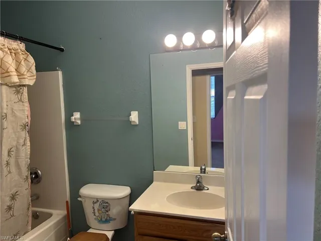 Bathroom featuring shower / bath combination with curtain, vanity, toilet, and a textured wall