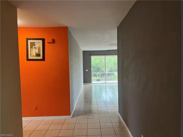 Hallway with light tile patterned floors, baseboards, and a textured wall