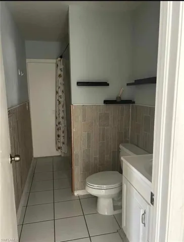Bathroom featuring wainscoting, vanity, a shower with shower curtain, light tile patterned floors, and tile walls