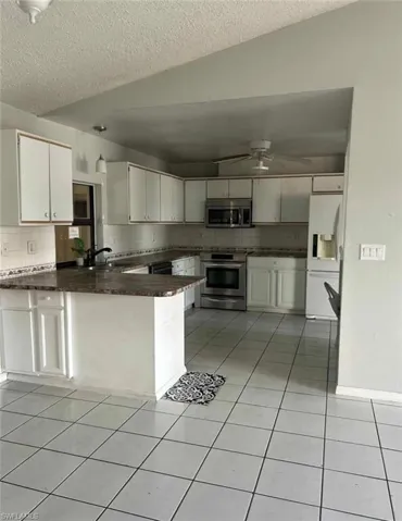 Kitchen featuring white cabinetry, a peninsula, stainless steel appliances, decorative backsplash, and light tile patterned floors