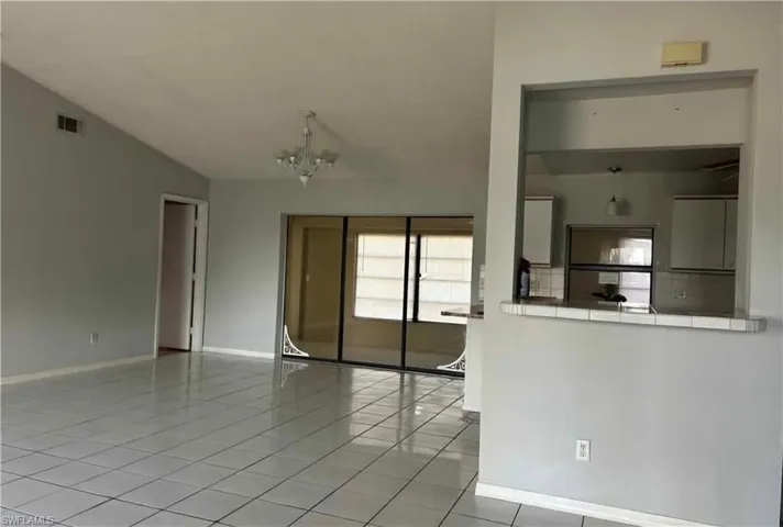 Unfurnished living room featuring light tile patterned flooring, a chandelier, and vaulted ceiling