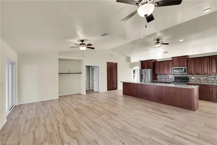 Kitchen featuring lofted ceiling, open floor plan, a large island with sink, appliances with stainless steel finishes, and light stone countertops
