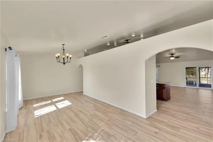 Unfurnished room featuring arched walkways, a ceiling fan, wood finish floors, and a chandelier