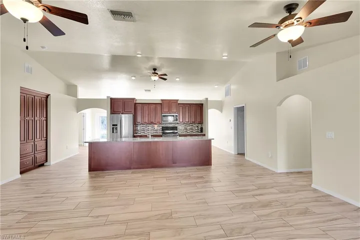 Kitchen featuring arched walkways, ceiling fan, stainless steel appliances, and high vaulted ceiling
