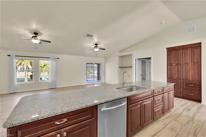 Kitchen featuring light stone counters, dishwasher, lofted ceiling, wood finish floors, and open floor plan
