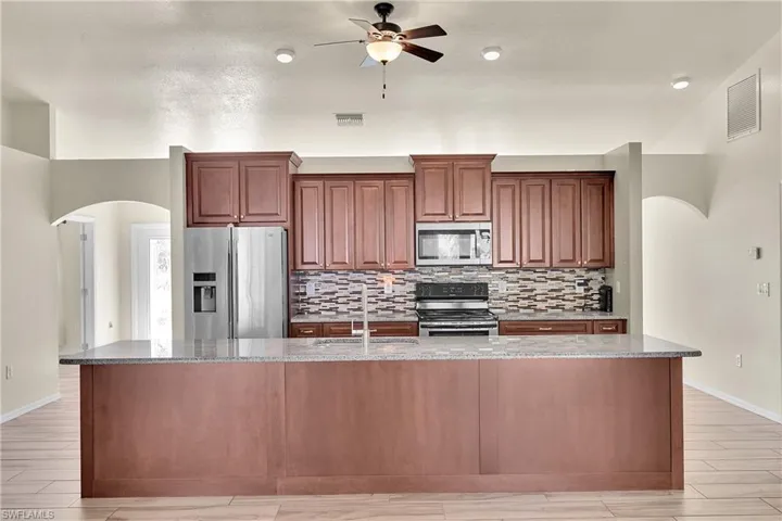 Kitchen with arched walkways, appliances with stainless steel finishes, light stone countertops, wood tiled floors, and a large island