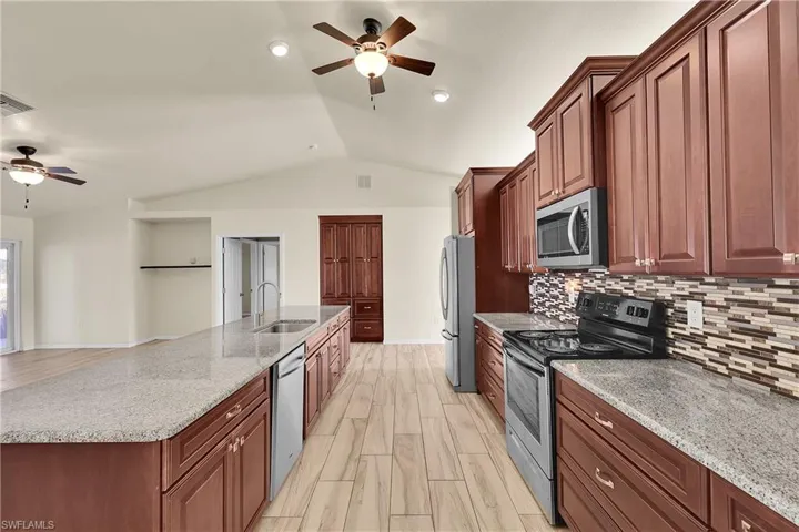 Kitchen featuring a ceiling fan, appliances with stainless steel finishes, lofted ceiling, light stone counters, and a large island