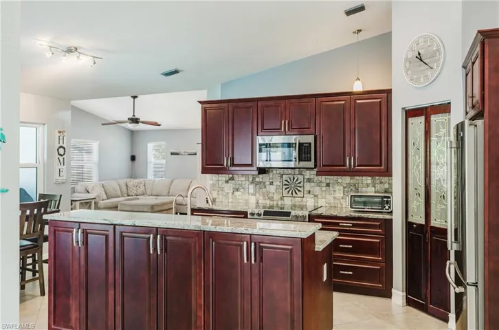 Kitchen featuring bold wood finish cabinetry, vaulted ceiling, ceiling fan, light stone counters, and open floor plan
