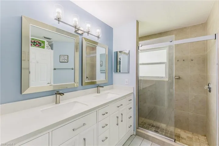 Full bath with double vanity, a shower stall, and light tile patterned floors