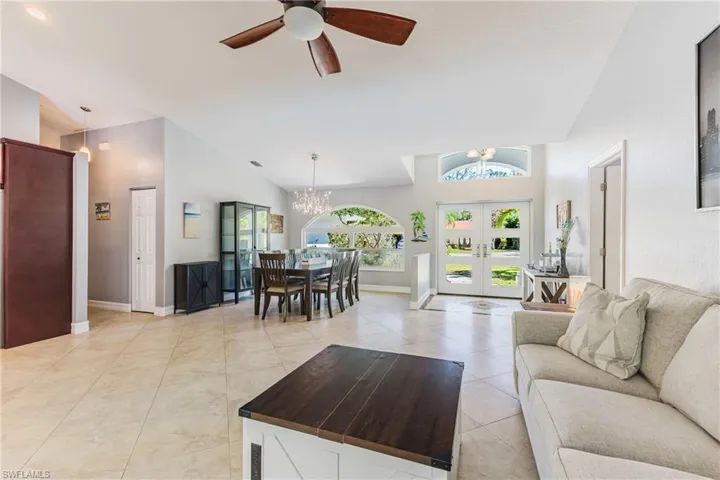 Living room featuring french doors, a chandelier, ceiling fan, light tile patterned floors, and vaulted ceiling