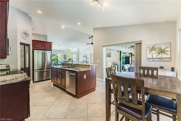 Kitchen with stainless steel appliances, light stone countertops, an island with sink, lofted ceiling, and reddish brown cabinets