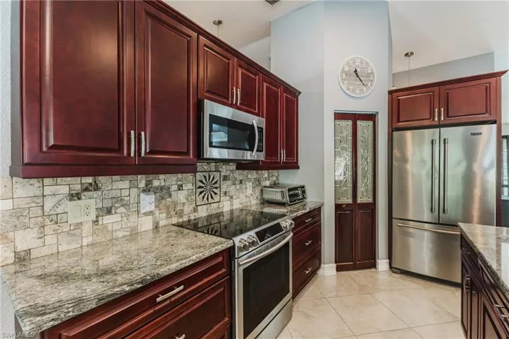 Kitchen featuring reddish brown cabinets, stainless steel appliances, light stone countertops, light tile patterned floors, and backsplash