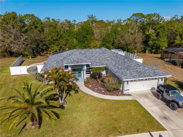View of front of property with driveway, an attached garage, a front lawn, and view of wooded area