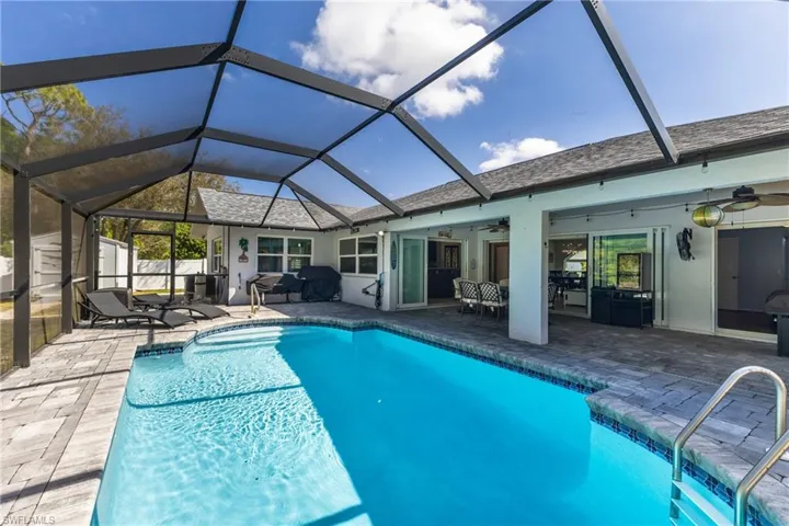 Swimming pool featuring a sunroom, a patio, outdoor dining area, and glass enclosure