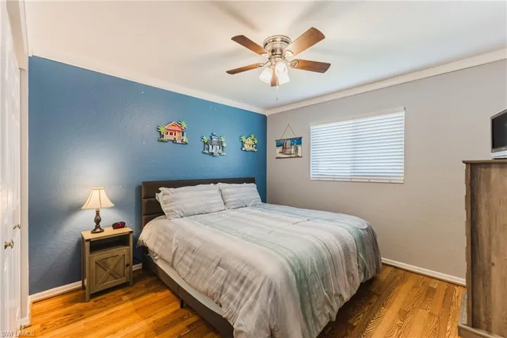 Bedroom featuring a textured wall, light wood-style floors, ceiling fan, and ornamental molding