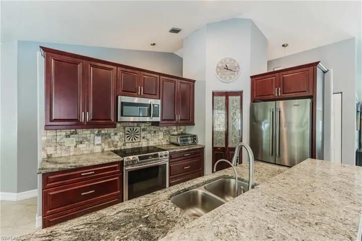 Kitchen featuring bold wood finish cabinets, stainless steel appliances, light stone countertops, vaulted ceiling, and tasteful backsplash
