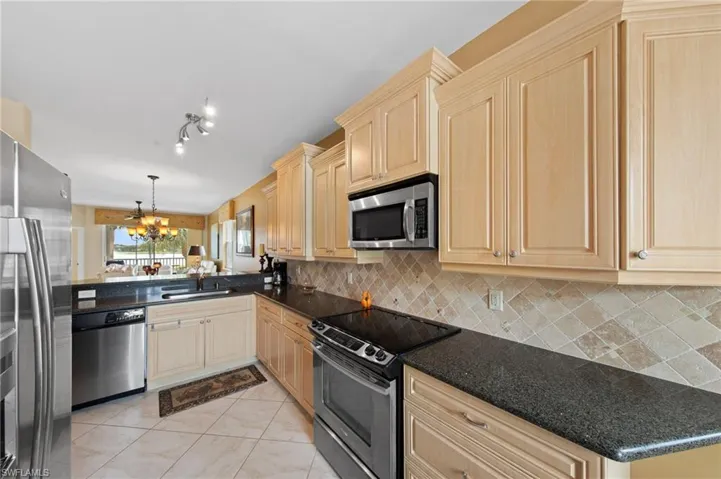 Kitchen with stainless steel appliances, light wood finish cabinetry, a chandelier, a peninsula, and tasteful backsplash