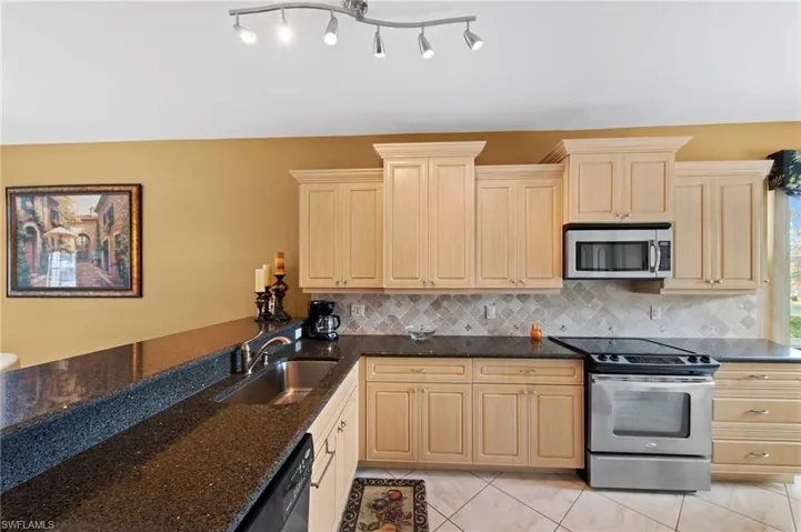 Kitchen with stainless steel appliances, dark stone countertops, and light wood finish cabinetry