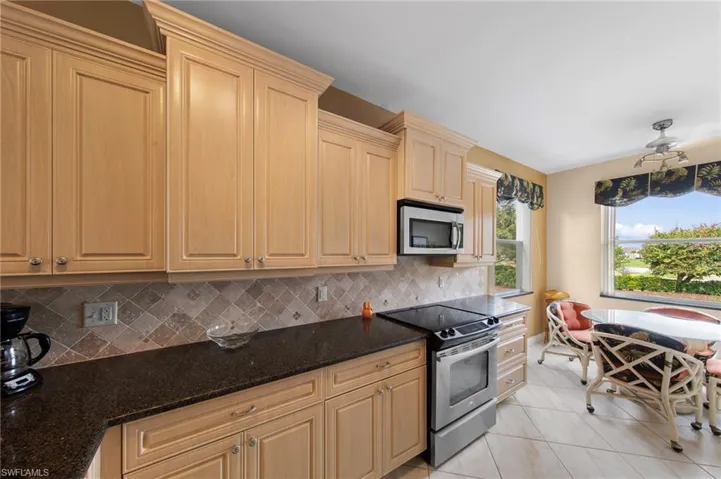 Kitchen featuring stainless steel appliances, dark stone countertops, light tile patterned flooring, light wood finish cabinets, and decorative backsplash