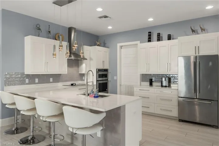 Kitchen with hanging light fixtures, tasteful backsplash, stainless steel appliances, exhaust hood, and white cabinets