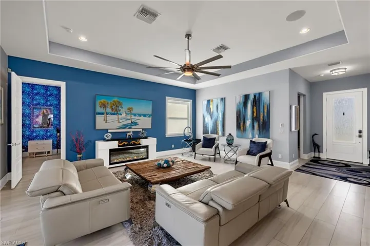 Living room featuring a raised ceiling, ceiling fan, a glass covered fireplace, and light wood-type flooring