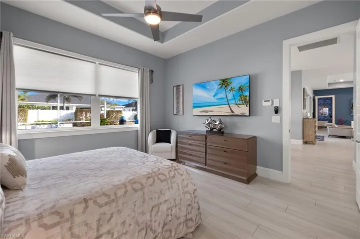 Bedroom with a raised ceiling, ceiling fan, and light wood-type flooring