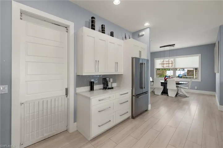 Kitchen with white cabinets, high end refrigerator, wood tiled floors, hanging light fixtures, and light stone countertops