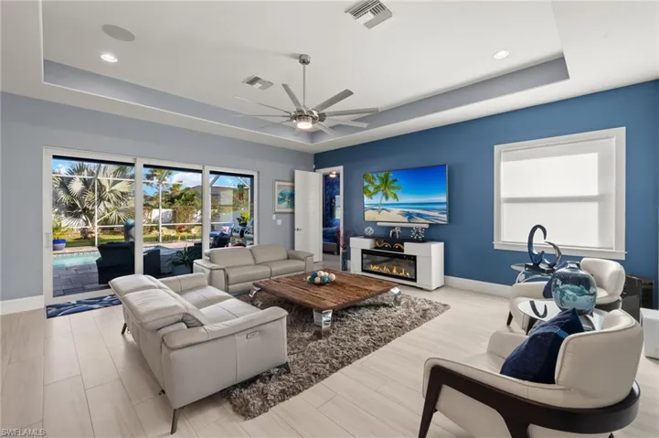 Living area with a raised ceiling, ceiling fan, light wood-style floors, a glass covered fireplace, and recessed lighting