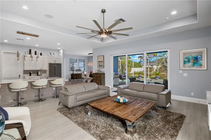 Living area with ceiling fan, recessed lighting, a raised ceiling, and light wood-style flooring